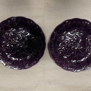 May include: Two purple ceramic plates with a raised floral design. The plates have a scalloped edge.