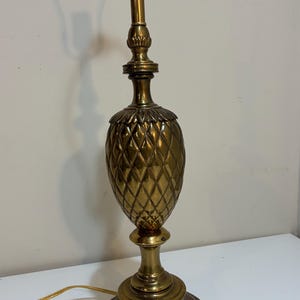 Puede incluir: Lámpara de mesa de latón con cuerpo en forma de piña y base redonda. La lámpara tiene un acabado dorado y un casquillo estándar. La lámpara mide aproximadamente 61 cm de altura.