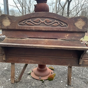May include: A vintage wooden bench with a carved design on the back and a shelf underneath. The bench is in need of restoration and has a rustic, weathered look.