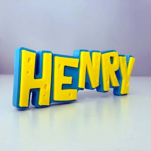 May include: A 3D-printed nameplate that spells out "HENRY" in bold, yellow letters against a blue background. The letters have a textured appearance, and the nameplate is likely a decorative item or a personalized gift.