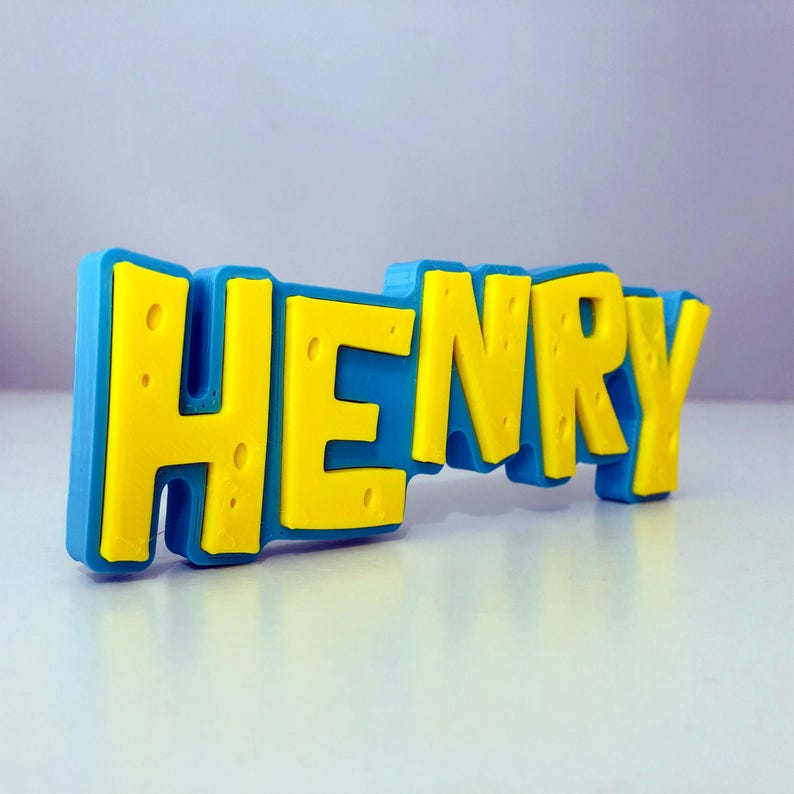 May include: A 3D-printed nameplate that spells out "HENRY" in bold, yellow letters against a blue background. The letters have a textured appearance, and the nameplate is likely a decorative item or a personalized gift.