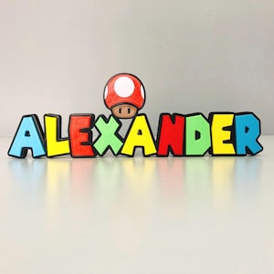 May include: A colourful wooden name sign with the name "ALEXANDER" spelled out in black outlined letters. A red and white mushroom character sits above the name.