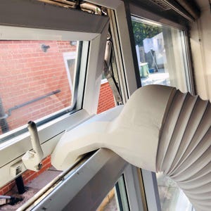 May include: A white plastic air conditioner exhaust hose adapter is securely fitted into an open white window frame. The flexible, ribbed white hose extends from the adapter, which is designed to vent hot air outdoors through the window opening.