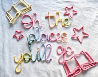May include: Colorful crocheted wall art spelling out "Oh the places you'll go" with star and book shapes. The letters and shapes are in shades of pink, yellow, green, and blue, creating a cheerful and whimsical design.