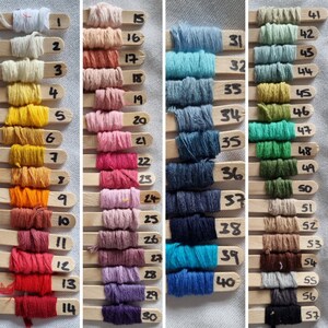 May include: A collection of 57 different colored embroidery floss spools, each wrapped around a wooden stick with a number label. The floss colors range from white to black, with shades of red, orange, yellow, green, blue, and purple.
