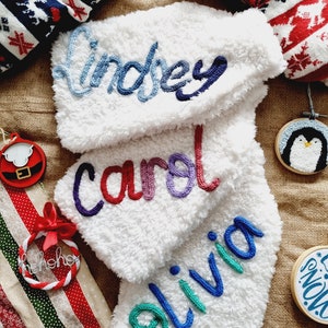 May include: Three white fluffy stockings with the names Lindsey, Carol and Olivia embroidered in colourful yarn.