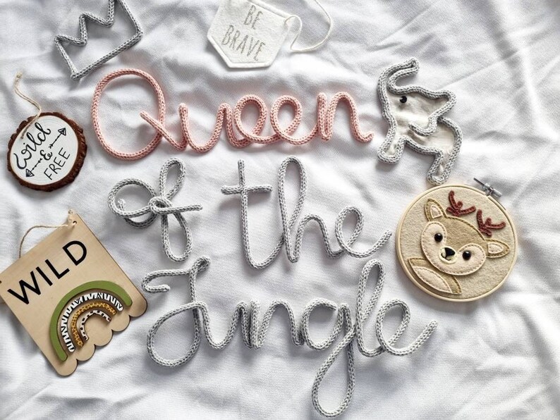 May include: A nursery decor set with the words "Queen of the Jungle" in pink and gray yarn. The set includes a crown, a deer, and wooden signs with the words "Wild" and "Wild & Free".