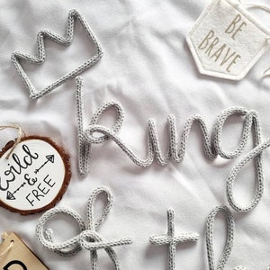 May include: A gray knitted word "king" with a gray knitted crown and a wooden sign with the text "wild & free" with an arrow.