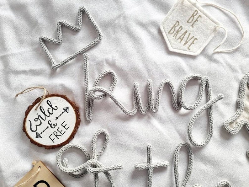 May include: A gray knitted word "king" with a gray knitted crown and a wooden sign with the text "wild & free" with an arrow.