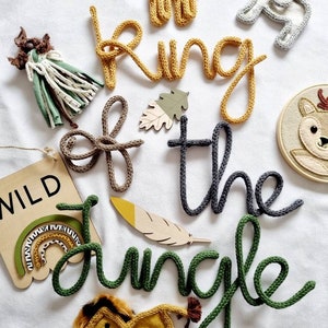 May include: A set of knitted word decorations spelling "King of the Jungle" in yellow, gray, and green. The decorations are surrounded by various animal-themed decorations, including a giraffe, elephant, lion, and rainbow.