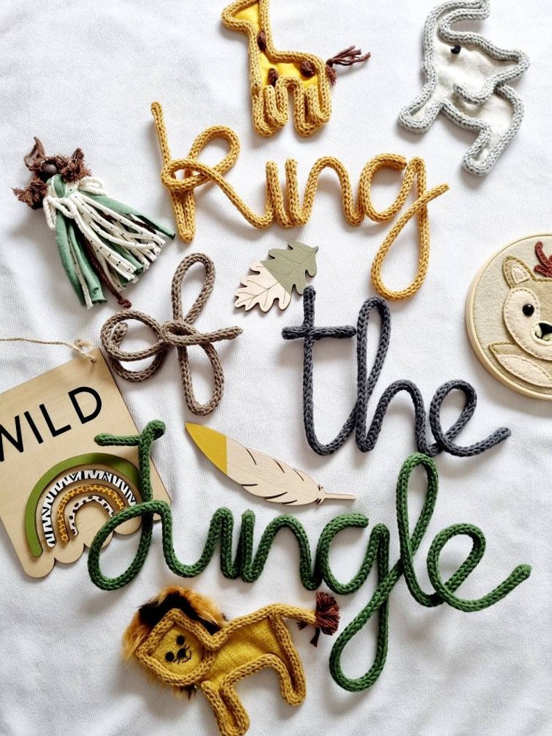 May include: A set of knitted word decorations spelling "King of the Jungle" in yellow, gray, and green. The decorations are surrounded by various animal-themed decorations, including a giraffe, elephant, lion, and rainbow.