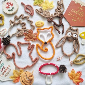 May include: An assortment of fall-themed crochet and fabric decorations, including a fox, owl, mushrooms, leaves, and a banner that reads "Autumn leaves and pumpkins please." The color palette includes orange, brown, and yellow.