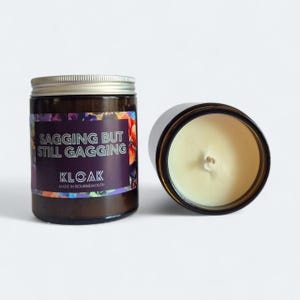 May include: Two brown glass jar candles with silver lids. One candle is upright, the other is on its side. The label reads "SAGGING BUT STILL GAGGING" and "KLOAK MADE IN BOURNEMOUTH". The candles have a creamy wax and a single wick.