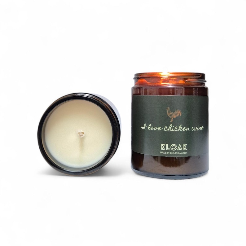 May include: Two glass jar candles, one open and one closed, with a white background. The closed candle has a dark green label with a rooster illustration and the text "I love chicken wine". The open candle is black with a white candle inside.