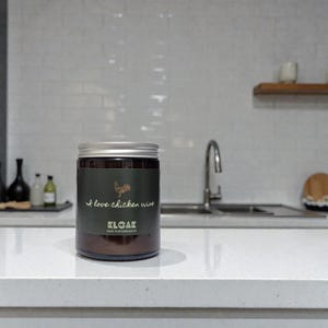 May include: A dark glass jar with a silver lid, featuring a green label with the text "I love chicken wine" and a rooster illustration. The jar is labeled "KLOAK" and "MADE IN BOURNEMOUTH".