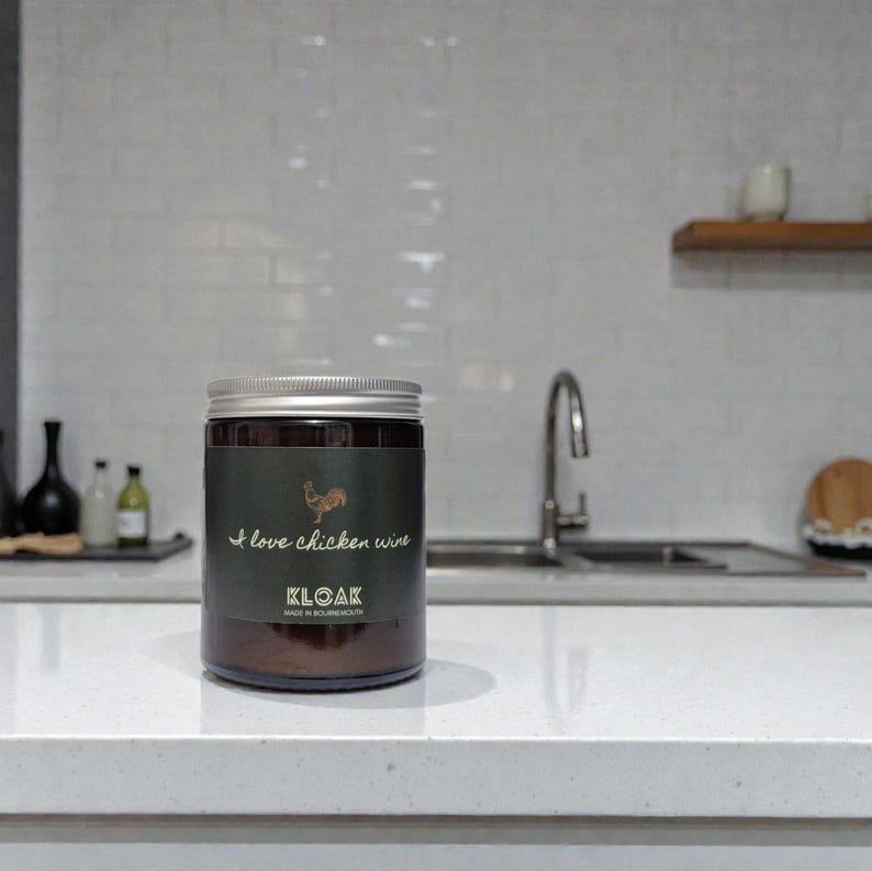 May include: A dark glass jar with a silver lid, featuring a green label with the text "I love chicken wine" and a rooster illustration. The jar is labeled "KLOAK" and "MADE IN BOURNEMOUTH".