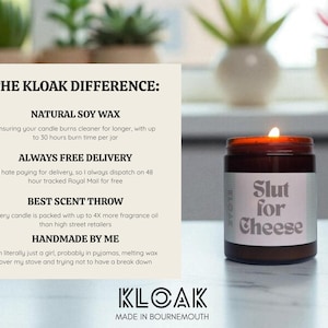 May include: A lit, brown glass jar candle with a white label that reads "Slut for Cheese." The candle is part of the KLOAK brand, which is handmade with natural soy wax and offers free delivery.