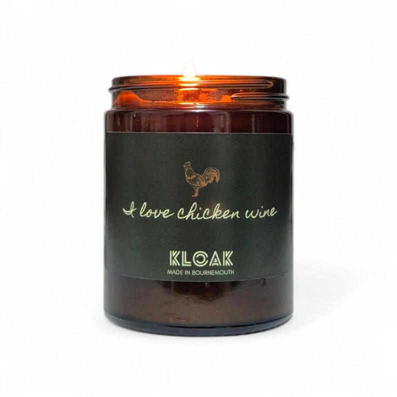 May include: A brown glass jar candle with a lit wick. The label reads "I love chicken wine" with a rooster illustration. The brand name "KLOAK" is printed below, with "MADE IN BOURNEMOUTH" underneath.