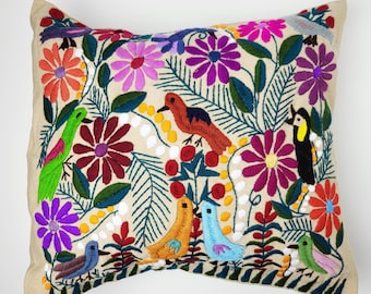 May include: Embroidered decorative pillow featuring colorful birds and flowers. The pillow has a beige background with vibrant embroidery in shades of red, purple, orange, green, and blue. The design includes various bird species and floral patterns.