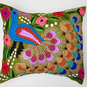 Könnte beinhalten: Besticktes Zierkissen mit einem Pfauenmuster. Das Kissen hat einen grünen Hintergrund mit einem bunten Pfau, Blumen und Blättern. Der Pfau ist blau, rot und lila, mit einem Fächerschwanz. Die Blumen sind rosa und rot.