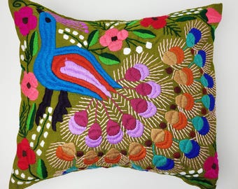May include: Embroidered decorative pillow with a peacock design. The pillow features a green background with a colorful peacock, flowers, and foliage. The peacock is blue, red, and purple, with a fanned tail. The flowers are pink and red.