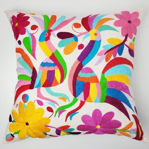 Peut inclure: Coussin carré blanc avec des broderies d'oiseaux et de fleurs. Les oiseaux ont un plumage coloré en rouge, orange, jaune, vert, bleu et violet. Des fleurs roses, jaunes et magenta sont également brodées sur le coussin.