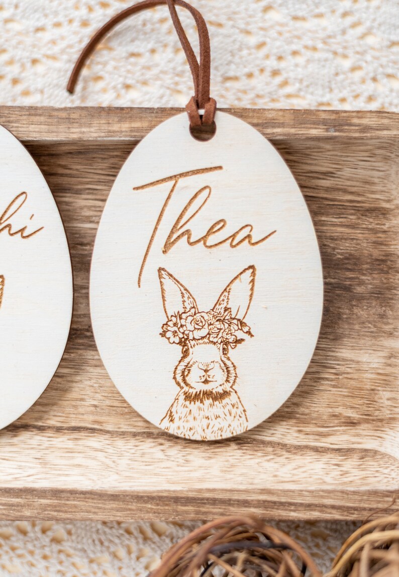 May include: A wooden Easter egg ornament with a bunny wearing a flower crown. The egg is engraved with the name "Thea".