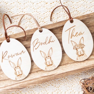 May include: Three wooden Easter egg ornaments with bunny illustrations and personalized names: Rowan, Bodhi, and Thea.