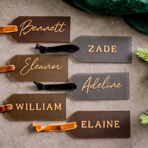 May include: Six brown and gray gift tags with gold lettering. The tags are tied with brown, black, and orange ribbon. The names on the tags are Bennett, Zade, Eleanor, Adeline, William, and Elaine.