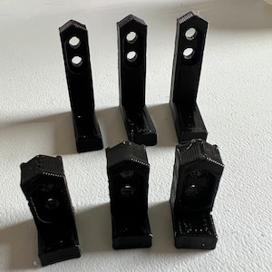May include: Six black plastic corner brackets with two holes each. The brackets are designed to be used for joining two pieces of wood or other materials at a 90-degree angle.