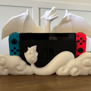 May include: A white 3D printed dragon figurine with wings outstretched, holding a Nintendo Switch console in its claws. The dragon is perched on a cloud-shaped base.