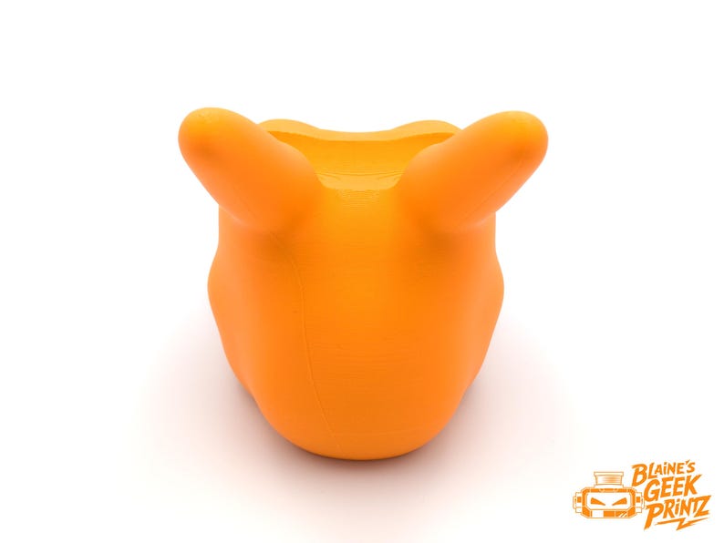 Op de afbeelding: Fel oranje 3D-geprint object met twee afgeronde uitsteeksels, die lijken op oren of handvatten, die omhoog steken. Het object heeft een gladde, matte afwerking en een afgeronde basis. De achtergrond is effen wit.