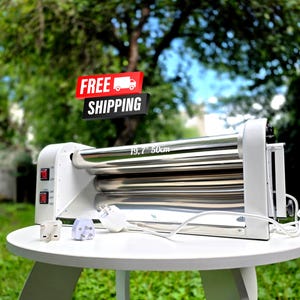 May include: A white electric laminator machine featuring two polished metal rollers and a control panel with two red power switches. The machine displays the text 19.7" 50cm on its surface and includes two white power plugs with different prong configurations.