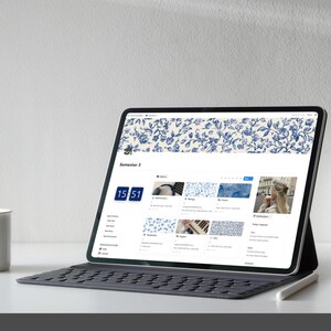 Peut inclure: Une tablette affiche une interface num&eacute;rique avec un motif floral bleu. L'&eacute;cran montre un calendrier et des ic&ocirc;nes d'applications. Une tasse blanche, un vase blanc et un stylet sont &eacute;galement visibles.