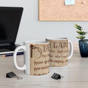 May include: Two white ceramic mugs with a historical manuscript design. The mugs feature a cream-colored background with faded brown text and illustrations, evoking a vintage aesthetic. The mugs are on a light-colored surface.