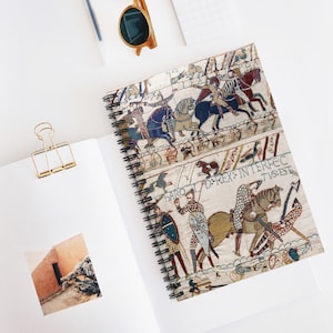May include: A spiral-bound notebook featuring a reproduction of the Bayeux Tapestry on its cover, depicting medieval soldiers on horseback and battle scenes with the Latin text HAROLD REX INTERFECTUS EST printed across the center of the design.