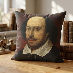 May include: A square throw pillow featuring a printed portrait of William Shakespeare. The image displays a man with dark hair, a mustache, and a beard, wearing a white collar and a dark garment against a deep reddish-brown background.