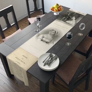 May include: A white table runner with a black and white illustration of Jane Austen and a quote from "Pride and Prejudice". The runner is on a dark wood table with two wine glasses and a plate of silverware.