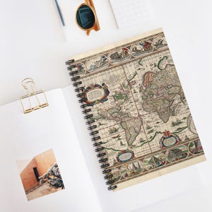 May include: A spiral-bound notebook featuring an antique-style world map on the cover, with detailed cartography, decorative borders, and Latin text. The notebook is open, revealing a white page with a small square photograph of a building.