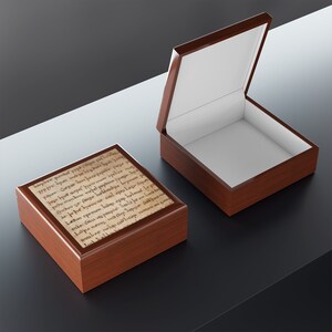 May include: A wooden box with a hinged lid. The lid is open and the inside of the box is lined with white felt. The box is decorated with a printed image of an old manuscript.