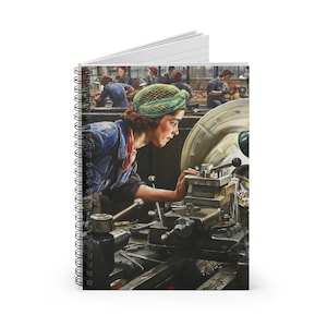 May include: A woman in a blue jumpsuit and a green hairnet operates a metal lathe in a factory setting. Other workers are visible in the background.