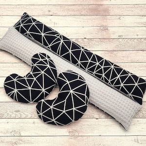 Könnte beinhalten: Eine Sammlung dekorativer Kissen in verschiedenen Formen. Die Kissen umfassen zwei nierenförmige Kissen und zwei lange Kissen. Die Kissen haben ein schwarzes geometrisches Muster auf weißem Hintergrund. Ein graues Kissen mit Waffelstruktur ist ebenfalls enthalten.