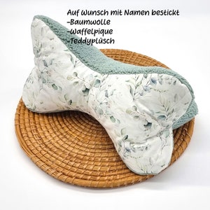 May include: A green and white patterned pillow with a soft, plush texture. The pillow is shaped like a bone and is perfect for cuddling. The pillow is made of cotton and teddy plush. The pillow is available in a variety of colours and patterns. The text on the pillow reads "Auf Wunsch mit Namen bestickt -Baumwolle -Waffelpïque -Teddyplüsch"