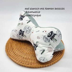 Könnte beinhalten: Ein weißes und grünes Kissen mit einem Waschbär-Druck. Das Kissen ist knochenförmig und hat eine Waffelpiké-Struktur. Der Text "auf Wunsch mit Namen bestickt - Baumwolle - Waffelpïque" ist auf das Kissen gedruckt.