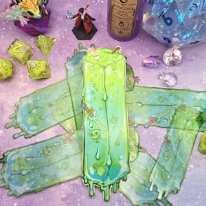 May include: A collection of fantasy-themed items, including a green, dripping, rectangular sticker with a sword and skull design. Other items include dice, a miniature figure, and a purple potion bottle labeled "Invisibility Potion."