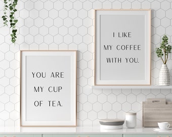 May include: Two framed art prints with the phrases "YOU ARE MY CUP OF TEA" and "I LIKE MY COFFEE WITH YOU" in black text. The prints are displayed on a white countertop with a mint green cabinet and a white hexagon tile backsplash.