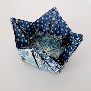 May include: A blue and white origami paper bowl with a floral pattern. The bowl is folded into a unique shape, creating a decorative and functional piece.