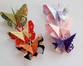 May include: A collection of six origami butterflies crafted from patterned paper. The butterflies feature various colors including green, red, orange, pink, purple, and white, with intricate floral and geometric designs on their wings.