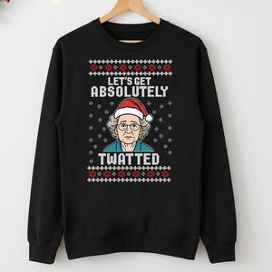 Może przedstawiać: Czarna bluza z świątecznym wzorem. Grafika przedstawia kobietę w czapce Świętego Mikołaja z białym napisem "LET'S GET ABSOLUTELY TWATTED". Czerwone i białe wzory płatków śniegu i kwiatów znajdują się u góry i u dołu.