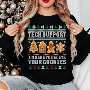 May include: Black sweatshirt featuring a Christmas-themed design. The text "TECH SUPPORT" and "I'M HERE TO DELETE YOUR COOKIES" are above and below gingerbread house, tree, man, and snowflake graphics.